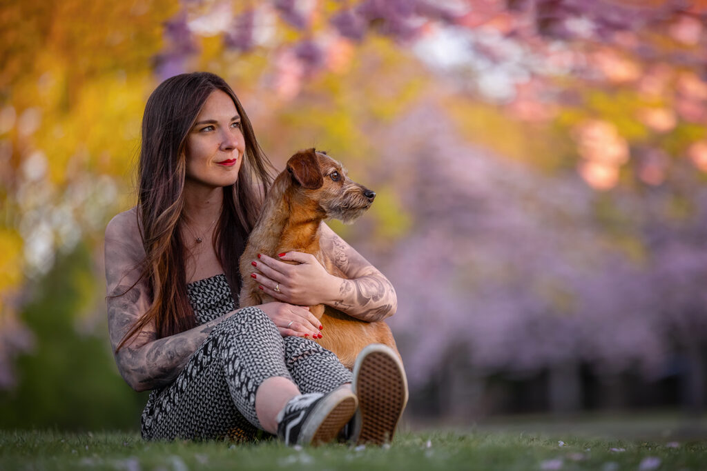 Eine Frau mit ihrem geliebten Terrier Rüden sitzt in Münster (NRW) auf einer Wiese unter blühenden Kirschbäumen, fotografiert von der Hundefotografin Anne Bertling aus Ascheberg im Münsterland.