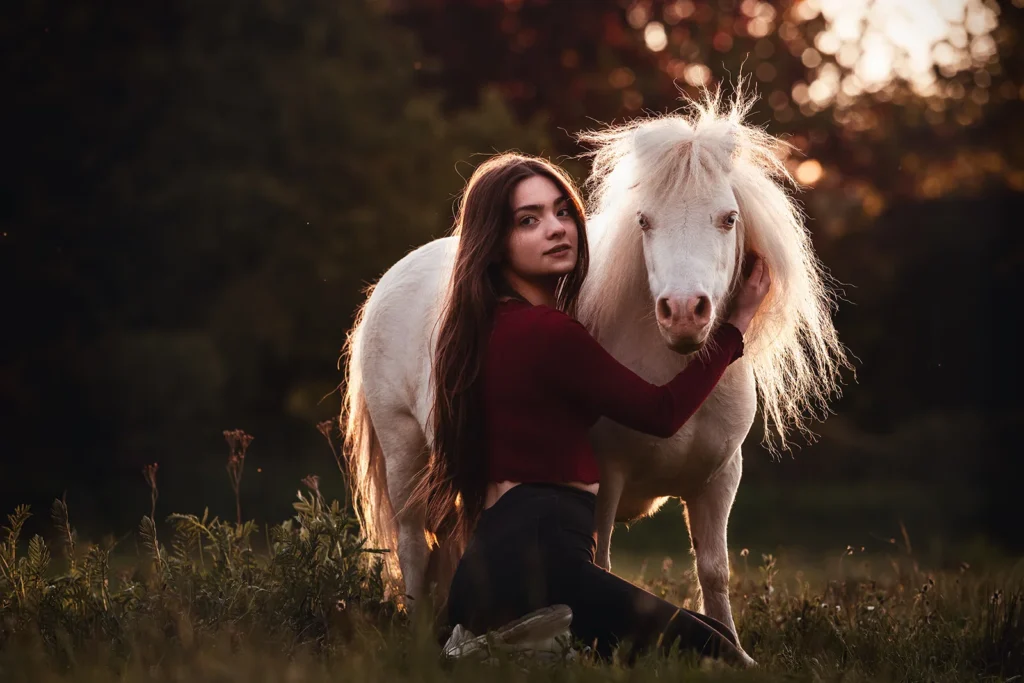 Inniges Kuschel Foto von einem weißen Shetland Pony und einer jungen Frau, sehr ausdrucksstark und naturnah, aufgenommen auf einer Weide im Ruhrgebiet (NRW) bei einem Ponyshooting durch die Pferdefotografin Anne Bertling aus Ascheberg bei Münster im Münsterland.