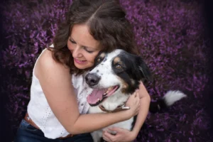 Eine Frau und ihr Border Collie sitzen kuschelnd in der Heide. Das Kuschelfoto wurde bei Coesfeld im Münsterland aufgenommen von der Hundefotografin Anne Bertling aus Ascheberg bei Münster.